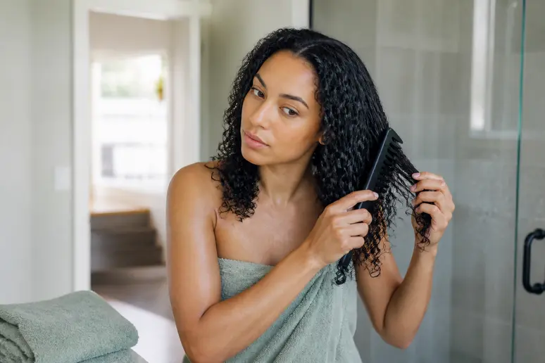 Une femme démêle ses cheveux frisés mouillés avec un peigne à dents larges, un soin protecteur pour la fibre capillaire appliqué.