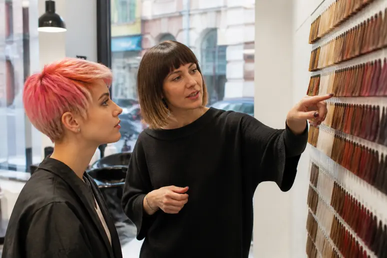 Une jeune femme discute avec son coiffeur à Lille, examinant des échantillons de couleur pour une nouvelle teinte.