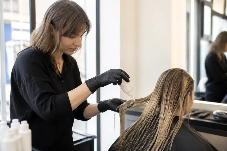 Une coiffeuse applique un soin Olaplex sur les cheveux d'une cliente dans un salon lumineux de Paris.