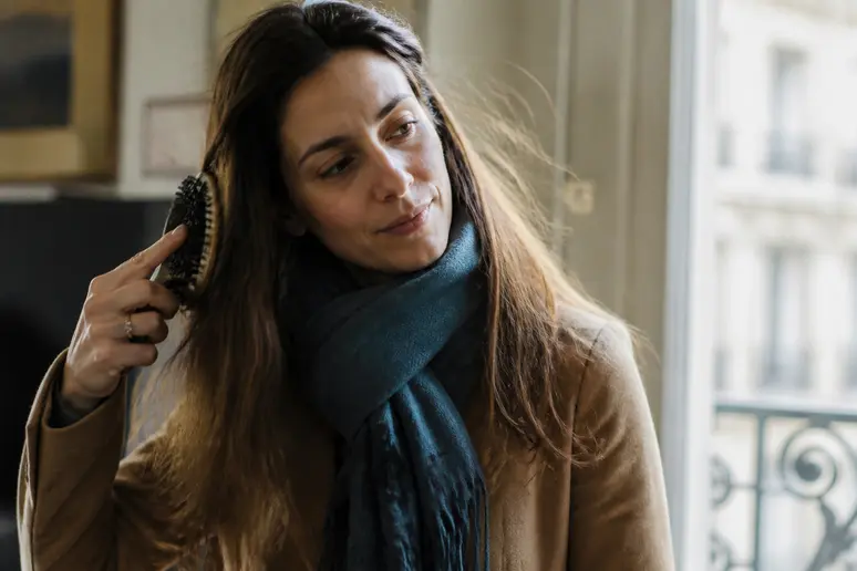 Une femme aux cheveux-électriques s'ébouriffent légèrement lors du brossage dans un intérieur lumineux.