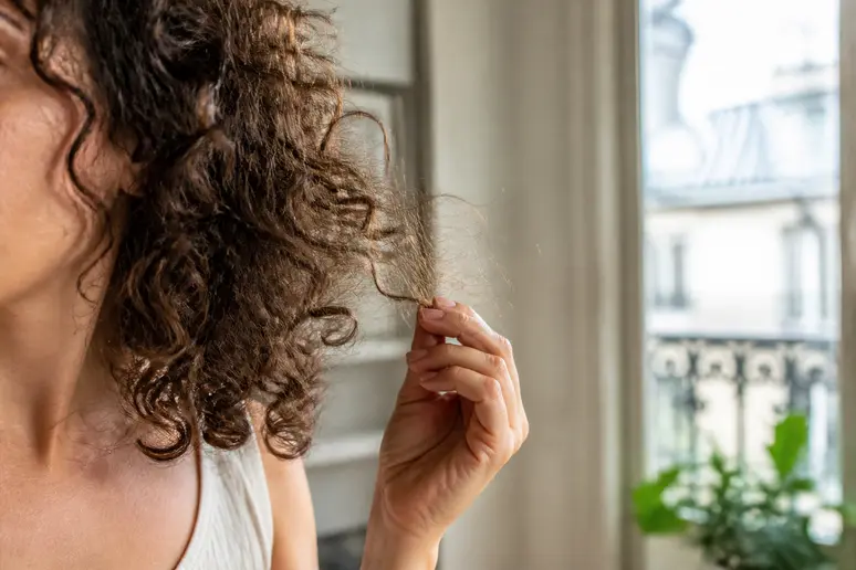 Une femme examine ses cheveux frisés, cherchant à comprendre comment coiffer cheveux frisés sans frisottis.