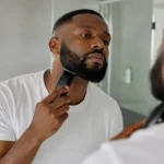 Collier de barbe : visage rond ou carré ? Un homme soigneusement taillé son collier de barbe devant un miroir de salle de bain lumineuse