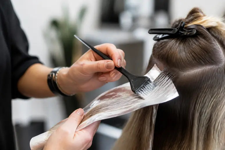 Coiffeur coloriste appliquant une coloration mèche par mèche avec un pinceau professionnel en salon