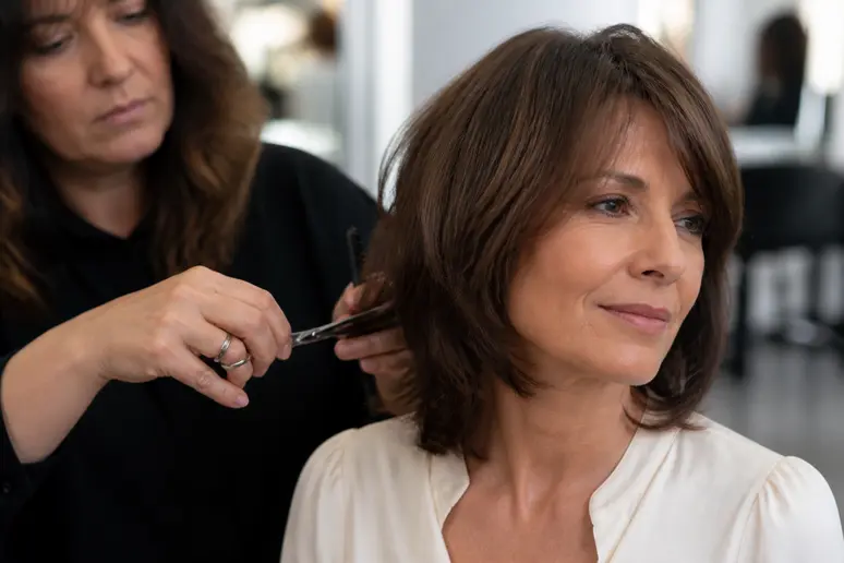 Coupe cheveux mi long dégradé effilé avec frange 50 ans : coiffeur ajustant la coupe sur une femme.