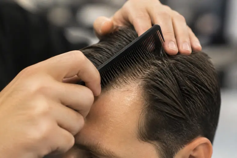 Mains utilisant un peigne fin pour gominer les cheveux en arrière de manière nette.