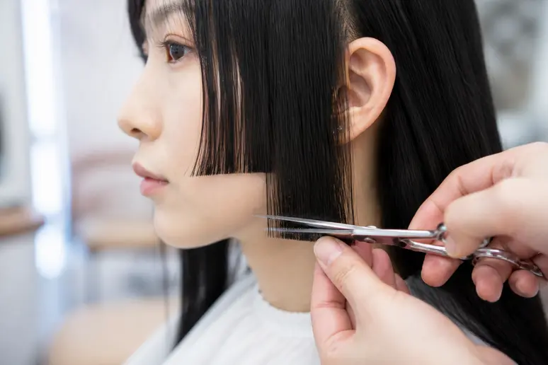Coupe précise des mèches latérales d'une hime cut longue par un coiffeur