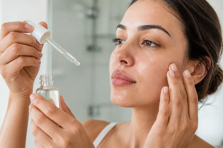 Application minutieuse d'un sérum fluide sur le visage lors de la routine de soins.