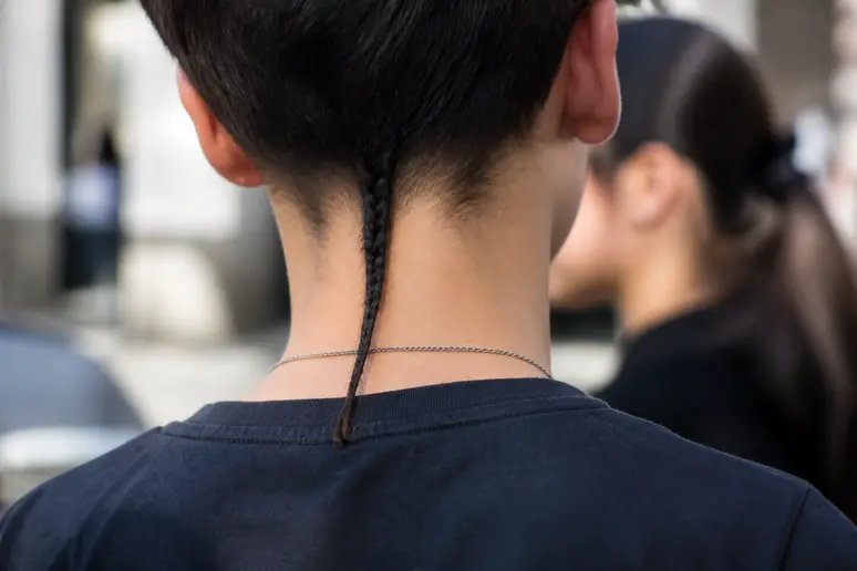 Jeune personne avec une coupe courte et une mèche fine de queue de rat sur la nuque.