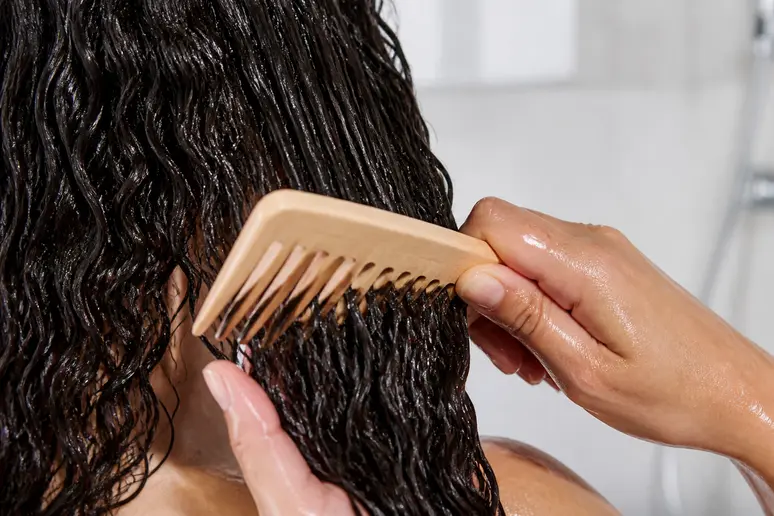 Mains démêlant délicatement des cheveux bouclés humides avec un peigne à dents larges.