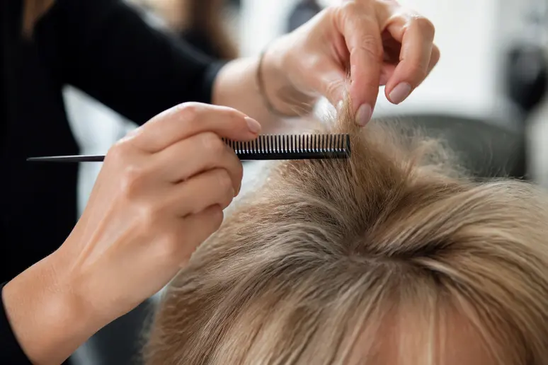 mains d'un coiffeur utilisant un peigne pour crêper délicatement les racines vers le bas